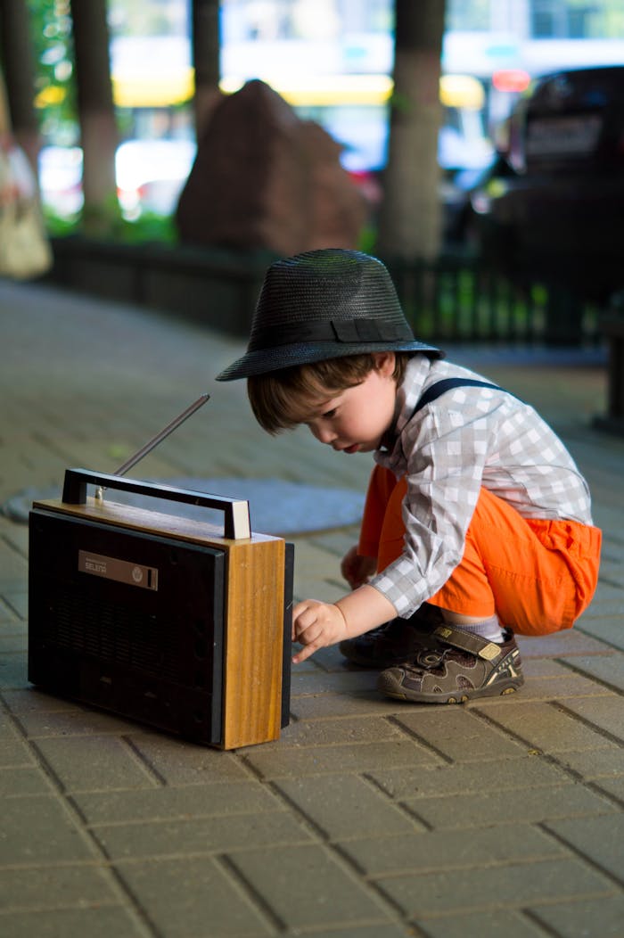 Home A young boy in fashionable attire adjusts an old-fashioned radio outdoors.
